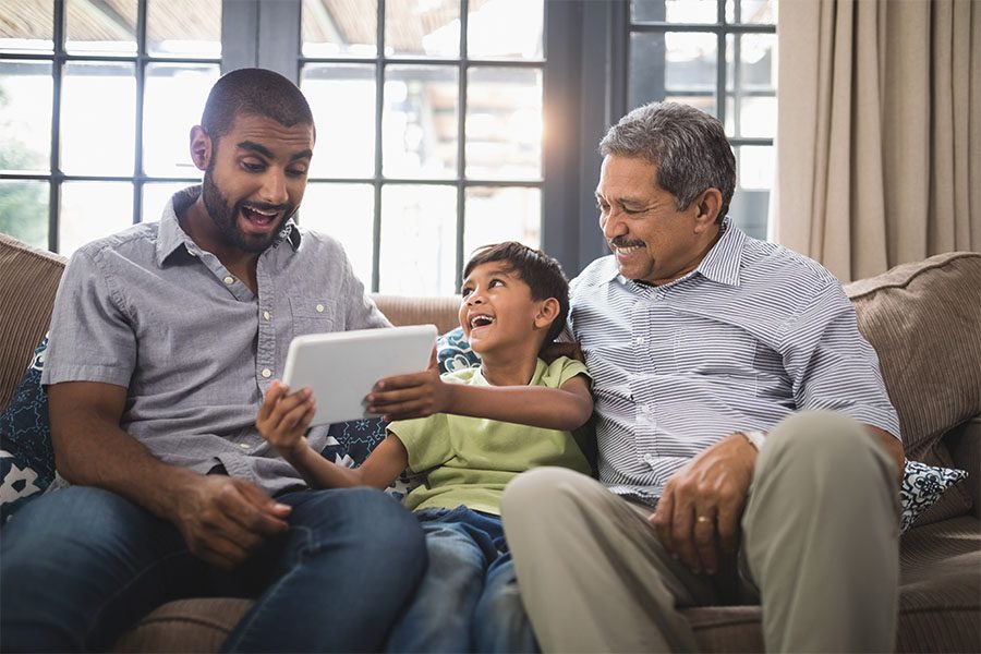 Client Center - Portrait of Cheerful Father and Grandfather Sitting on the Sofa While a Young Boy Shows Them His Tablet