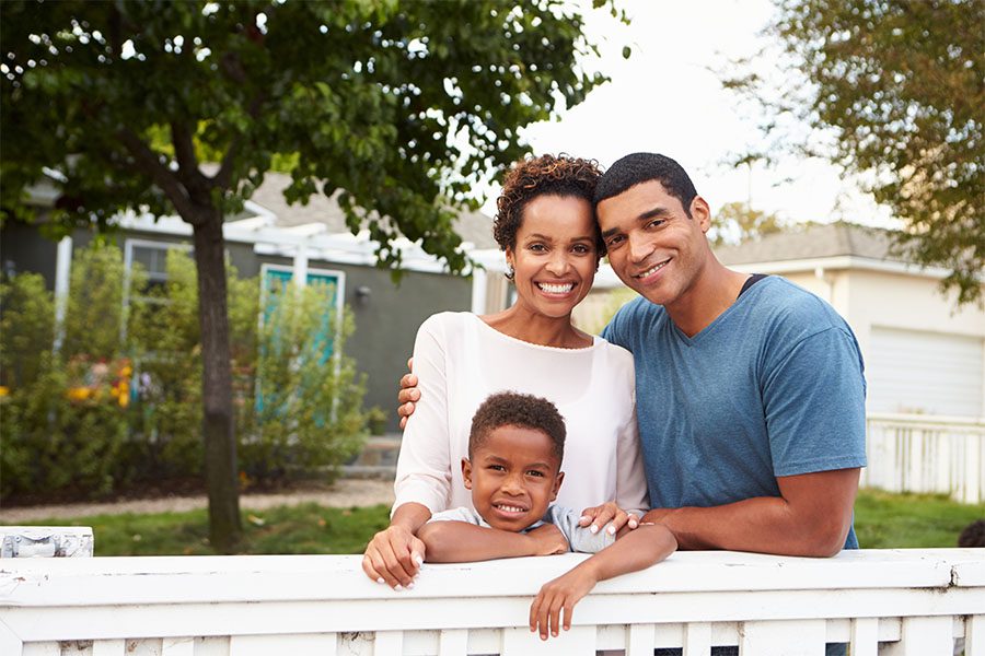 Personal Insurance - Portrait of Happy Family with a Young Son Standing Next to a White Picket Fence in Front of Their New Home